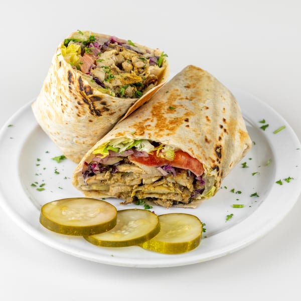 Two Falafel Hut chicken shawarma wraps, cut in half, with pickles on a white plate.