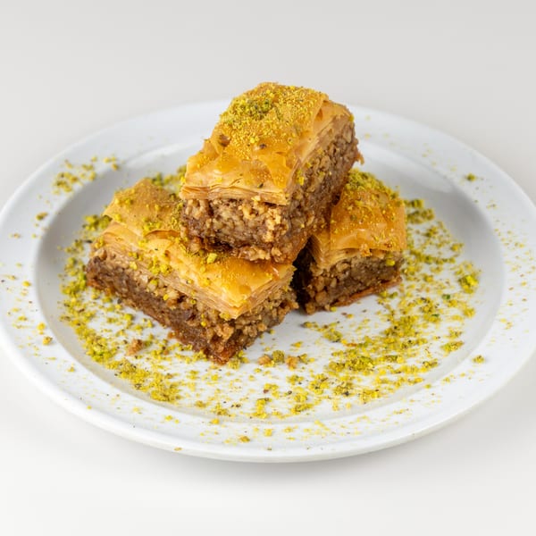Three pieces of baklava, topped with crushed pistachios, on a white plate.