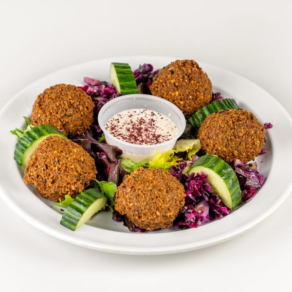 Falafel Hut's falafel plate with five crispy falafel, salad, cucumber slices, and a side of sauce.