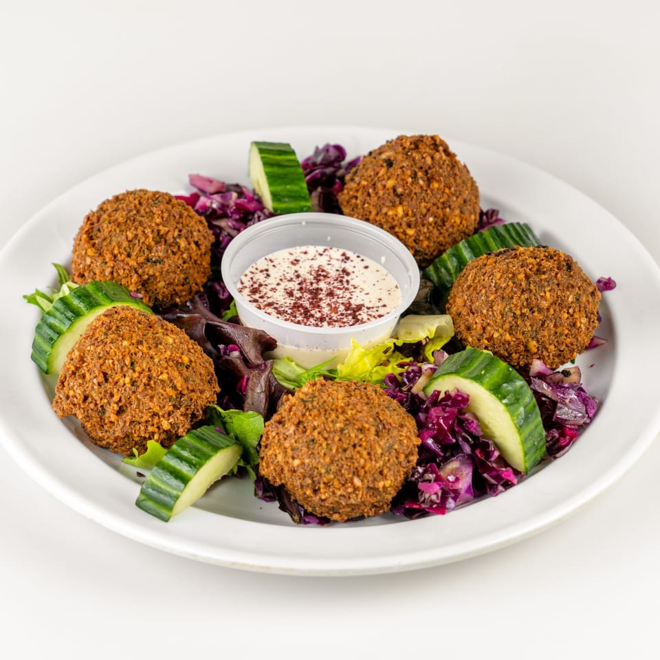 Falafel Hut's falafel plate with five crispy falafel, salad, cucumber slices, and a side of sauce.