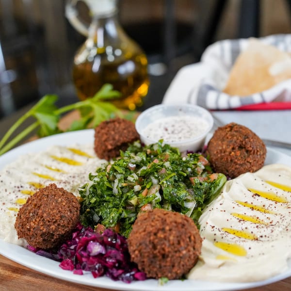 A Falafel Hut platter with falafel, hummus, tabbouleh, and pickled cabbage, with pita and olive oil in the background.