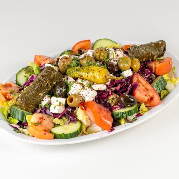 A vibrant Mediterranean salad with stuffed grape leaves, olives, feta, tomatoes, cucumbers, and peppers.